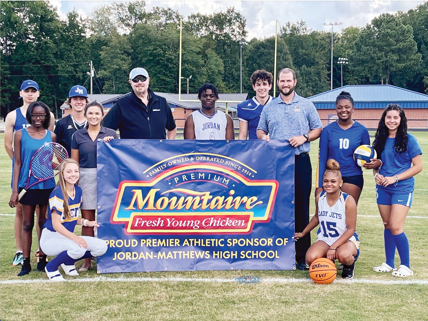 Mountaire's Sasha Duncan (holding banner, left) and Carl Barnes (beside Duncan) pose with Jordan-Matthews Athletic Director Josh Harris and athletes. Mountaire has become a premier sponsor of J-M's sports teams.