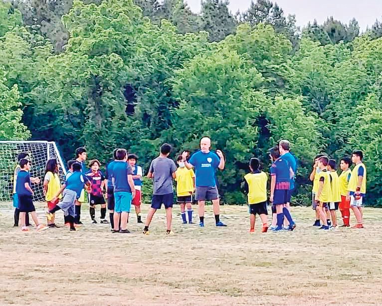 Siler City FC coach Chip Milliard (in blue, center) speaks with players trying out for the club's boys travel soccer teams in May.