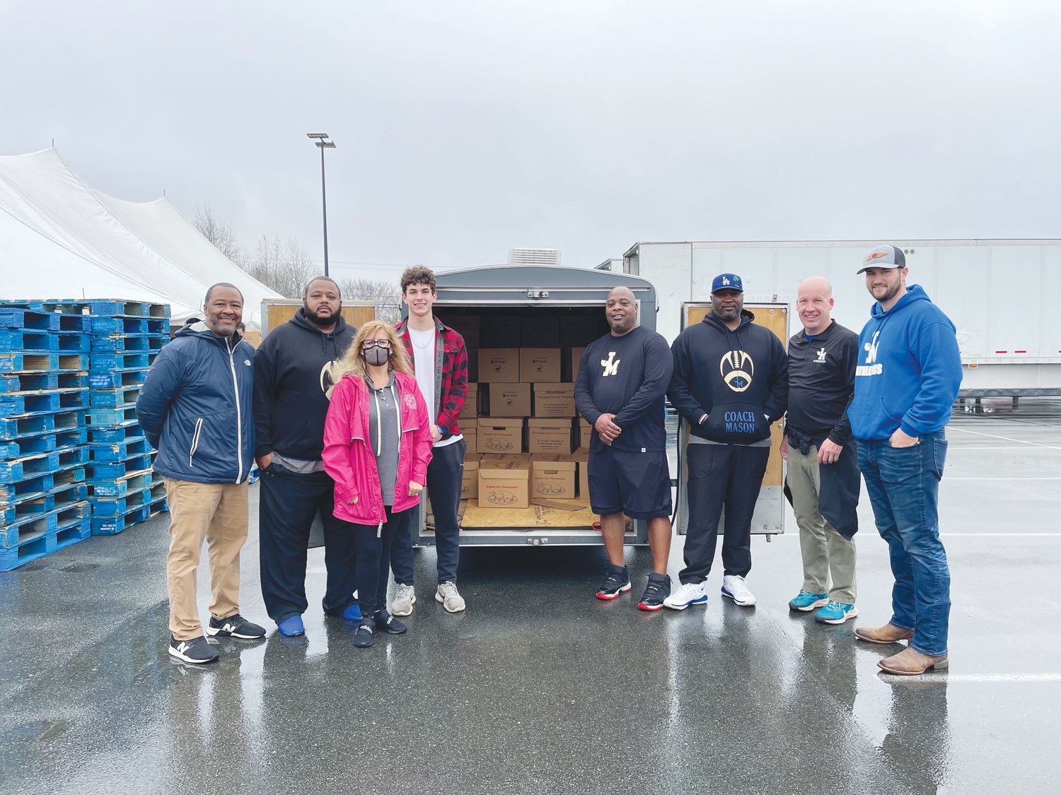 Jordan-Matthews volunteers (from left to right: Rodney Wiley, Ryan Johnson, Donna Barger (in pink), Calvin Schwartz, Kenyon Burns, Coach Mason, Chip Millard and Josh Harris) pose for a photo beside the loaded trailer full of holiday boxes from Mountaire for their 'Christmas for Thousands' giveaway on Dec. 11.