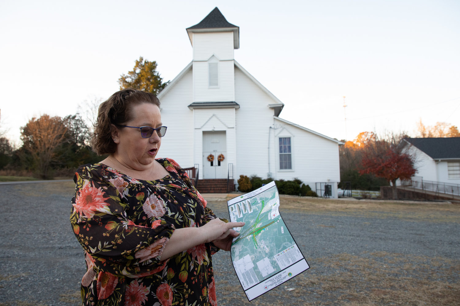 Sharron Bouquin, 60, stands in front of Merry Oaks Baptist Church with the maps of proposed roadway plans from N.C. Dept. of Transportation. The church is slated to be taken by NCDOT to make way for the new VinFast manufacturing facility in Moncure.